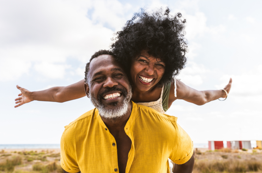 Happy smiling couple, both with straight wight teeth. Laughing as the lady sits on the man's back and stretches her arms wide